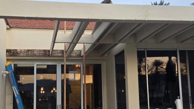 Worker inspecting rotted patio cover beam demolition Palm Desert